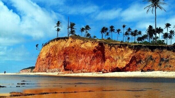 A beach with a large reddish cliff and palm trees. - House in Cumuruxatiba prox. Cliffs, mezzanine and spacious suite, sea view  (Prado)