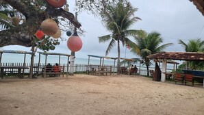 A beachside area with wooden benches and tables, palm trees, and a view of the sea. - House in Cumuruxatiba prox. Cliffs, mezzanine and spacious suite, sea view  (Prado)