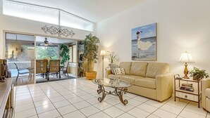 Ein geräumiges Wohnzimmer mit einem Glastisch, einem beigefarbenen Sofa und einem Essbereich mit Korbmöbeln.