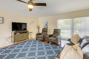 A living room with a television, two leather chairs, a sofa, a patterned rug, and a ceiling fan.