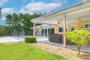 Uma área de varanda coberta com mobiliário de jardim, piscina e um quintal cercado.
