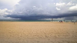 A beach with a sandy shore, a few beach chairs, and umbrellas under a cloudy sky. - Riviera Beach Vacation Home w/ Pool: Walk to Beach (Riviera Beach)
