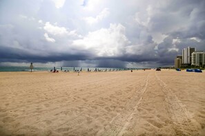 A beach with a sandy shore, a few umbrellas, and a distant view of buildings.