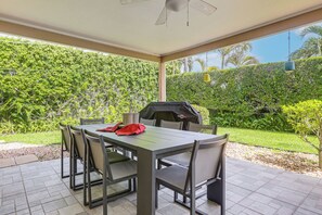 Eine Terrasse im Freien mit Tisch, Stühlen, einem Grill und Blick auf einen üppigen Garten.