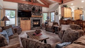A cozy living room with a stone fireplace, wooden beams, and a stone wall. - Large Luxury Family Home (Sunriver)