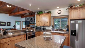 A modern kitchen with granite countertops, wooden cabinets, stainless steel appliances, and a large island with a sink. - Large Luxury Family Home (Sunriver)