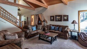 A cozy living room with wooden beams, a staircase, and a fireplace. - Large Luxury Family Home (Sunriver)