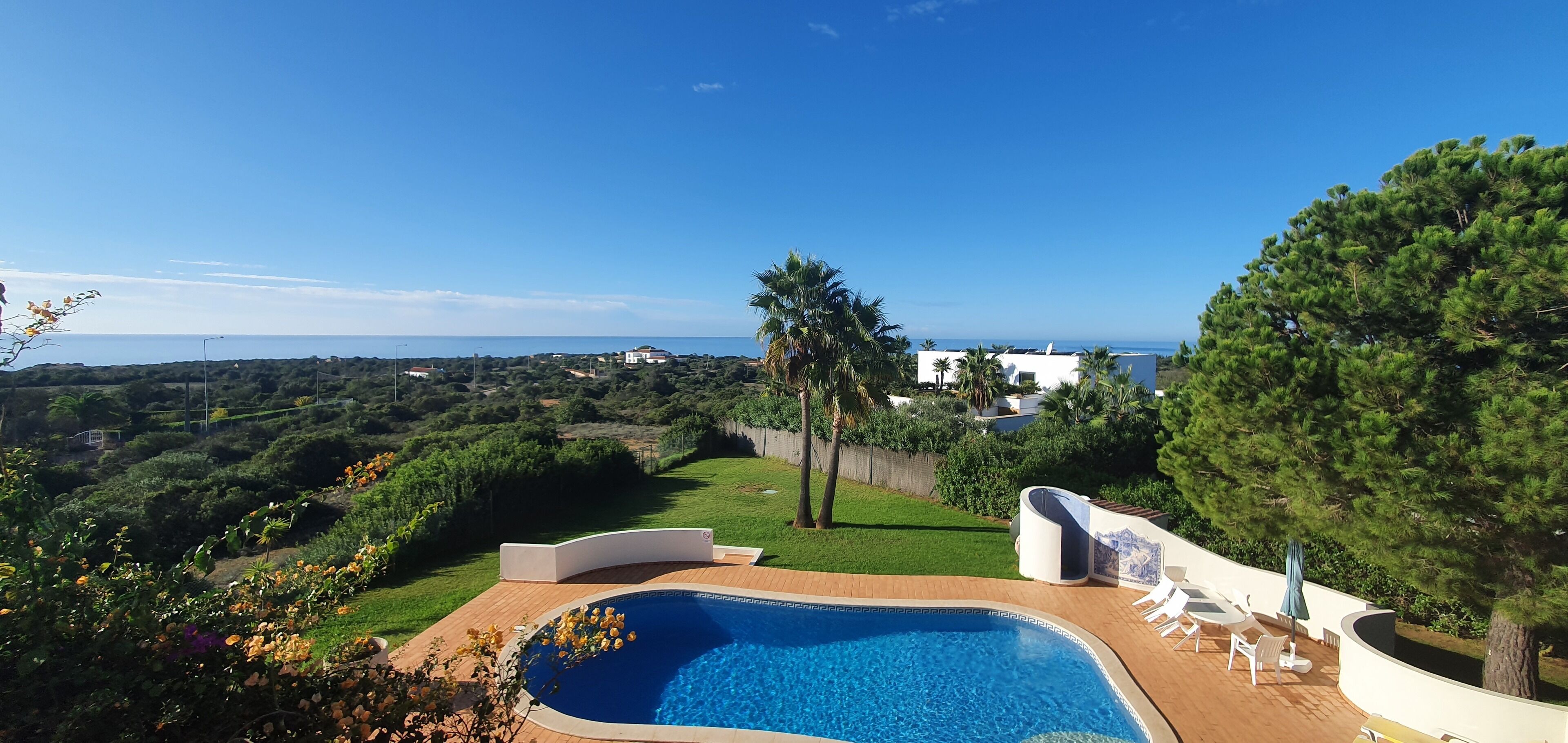 Ein Pool mit Blick auf das Meer, umgeben von Grünpflanzen und einem weißen Gebäude.