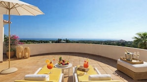 Un espace extérieur aménagé avec des sièges incurvés, des fauteuils confortables, une table avec des boissons et une vue sur la mer.