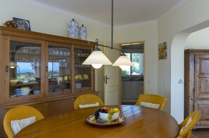 A dining area with a wooden table, yellow chairs, a fruit bowl, and a cabinet with glass doors. - Family‑Friendly Villa with Beautiful Sea Views, Private Pool & Spacious Gardens (Estômbar)