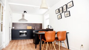 Une cuisine moderne avec un îlot central, des meubles noirs et un plan de travail en bois. On y trouve deux chaises marron autour de l’îlot et une suspension au-dessus.