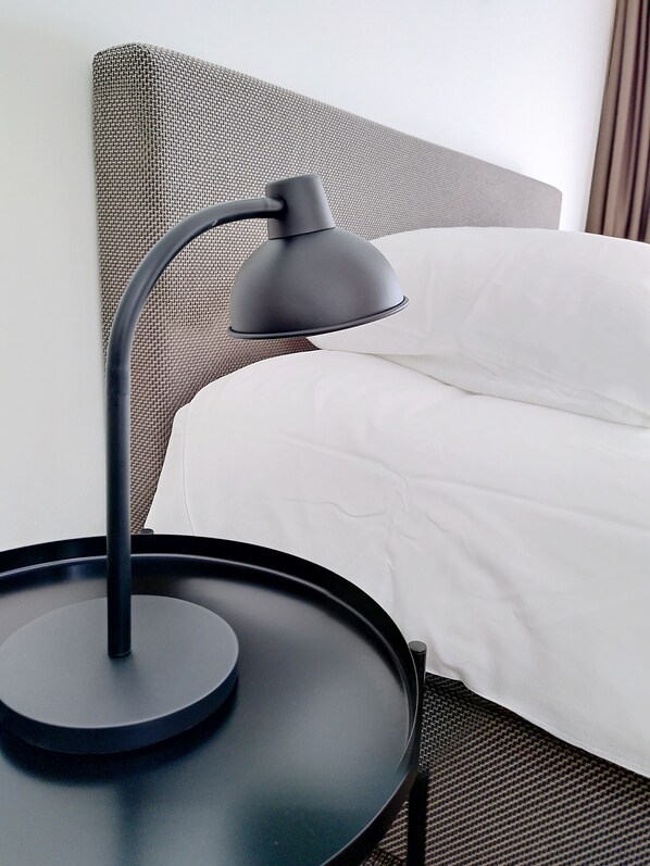 A bed with white bedding, a black table with a lamp, and a woven headboard.