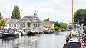 Un canal con barcos amarrados, un edificio con una torre de reloj y una hilera de casas a lo largo del agua.