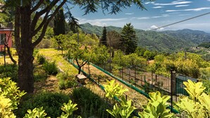 A lush garden with a variety of plants and trees, a fenced area, and a view of distant mountains. - Large Apartment in a splendid quiet area - seaview (Italia)