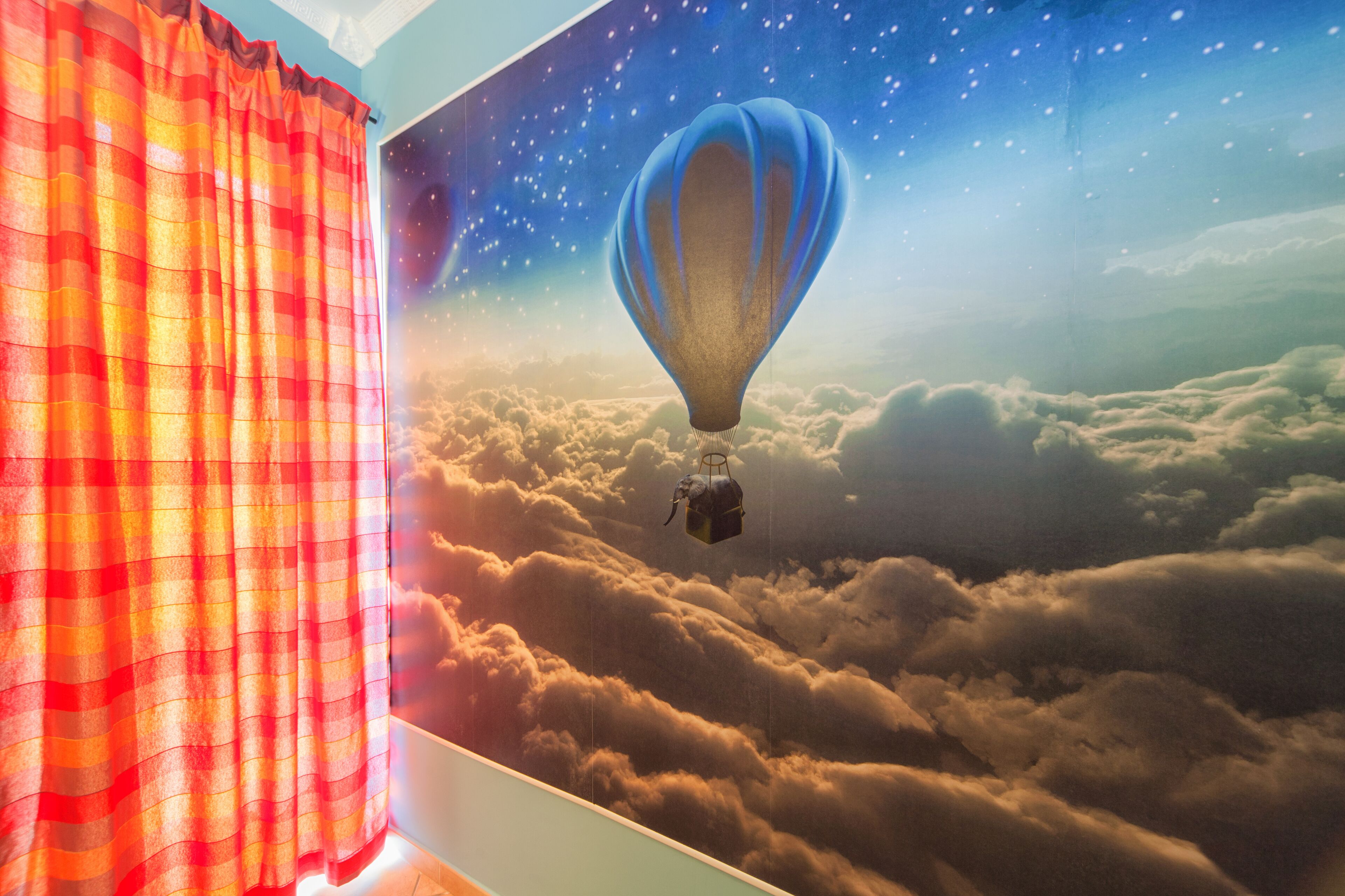 A room with a view of a hot air balloon over clouds through a window.