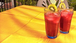 A table with a yellow tablecloth, two glasses of red beverage with kiwi slices, and a blue umbrella with fruit patterns. - Large Apartment in a splendid quiet area - seaview (Italia)