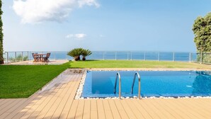 A swimming pool with a view of the sea, a wooden deck, and a table with chairs. - Villa Chimera by LovelyStay (Caniço)