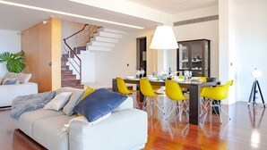 A modern living room with a sofa, yellow chairs, and a dining area with a table and chairs.