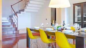 A modern dining area with a staircase, bright yellow chairs, and a large dining table set for a meal.
