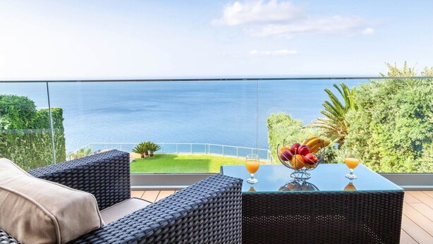 A balcony with wicker furniture, a glass table, and a fruit bowl. - Villa Chimera by LovelyStay (Caniço)