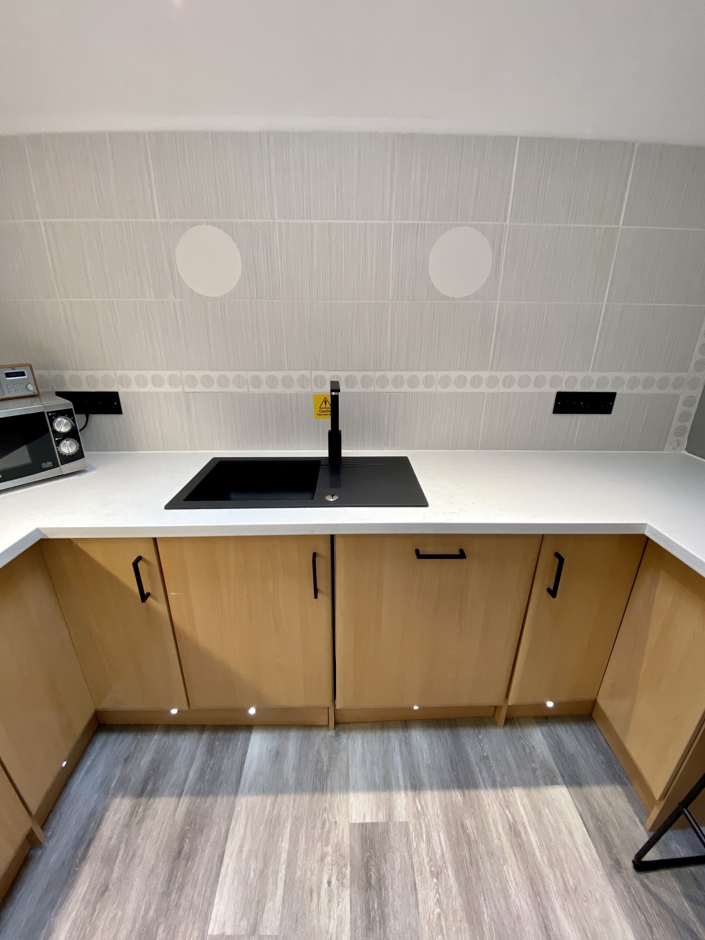 A modern kitchen with a white countertop, wooden cabinets, and a black sink.