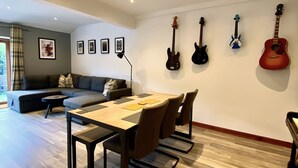 A modern living room with a dining area, a sofa, a coffee table, and a dining table with chairs. There are guitars hanging on the wall. - 3 Sheraton Apartments, Modern Luxury Apartment,Breathtaking Views of Ben Nevis (Fort William)