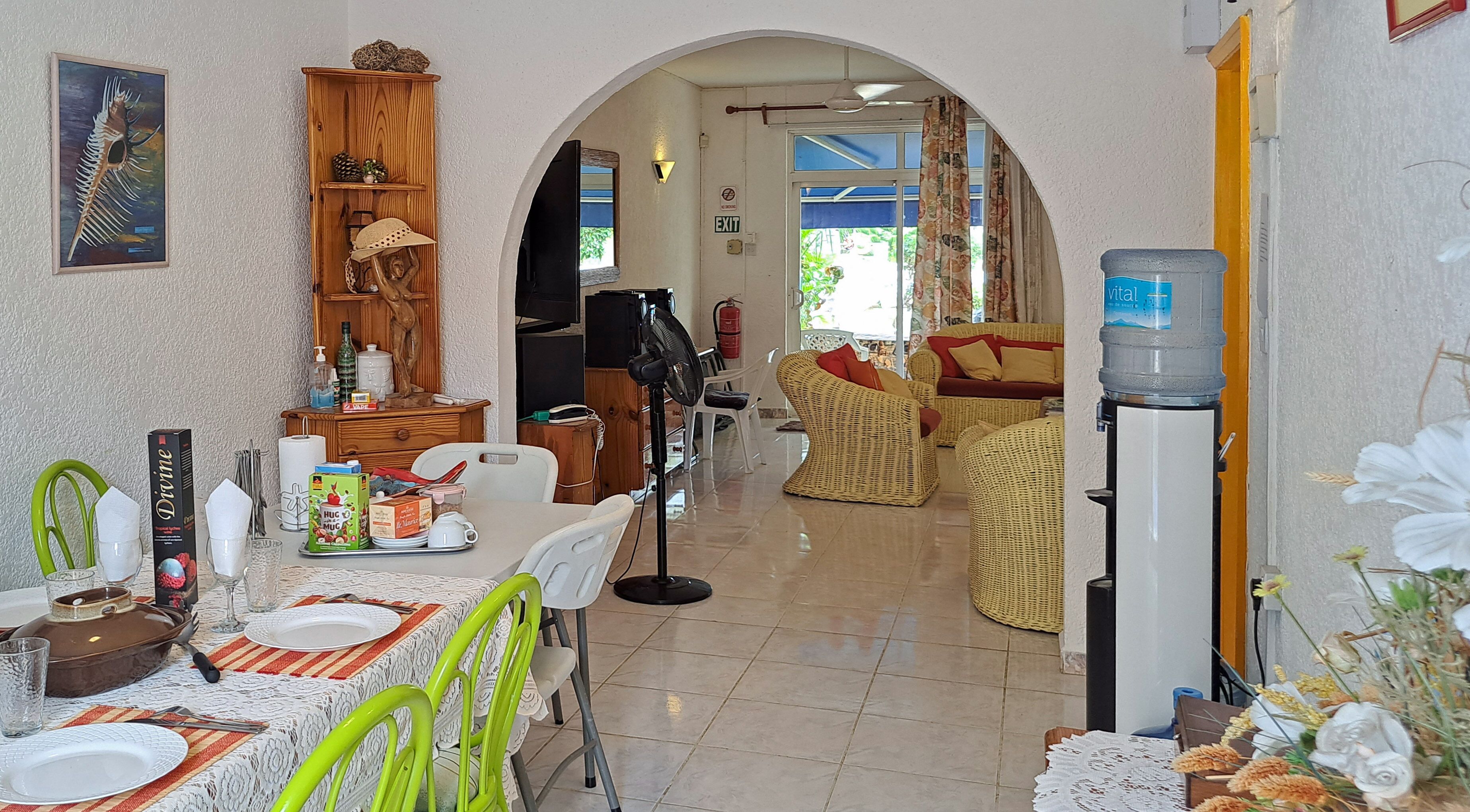 A dining area with a table set for two, a wicker sofa, and a water dispenser.