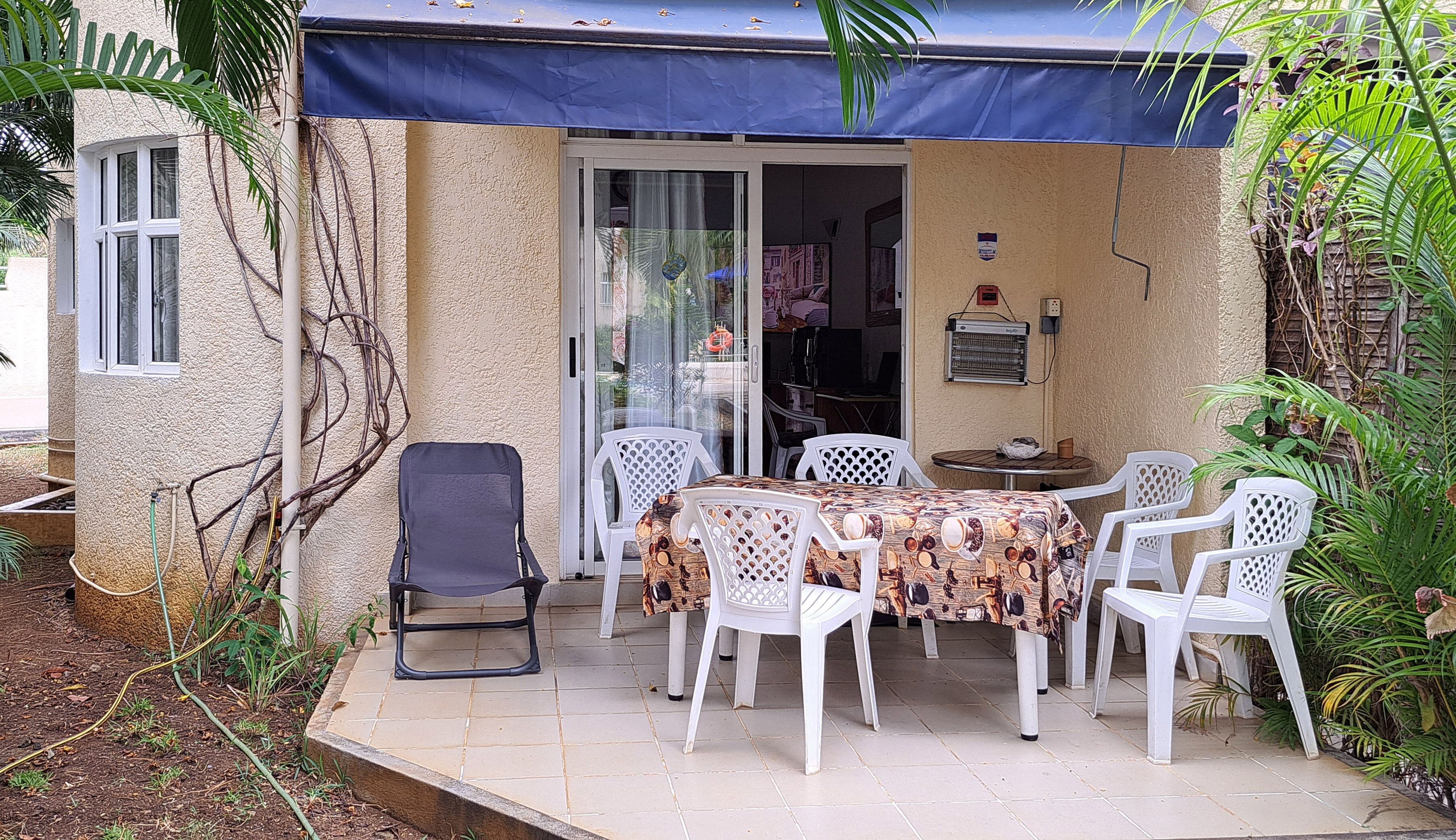 A covered outdoor seating area with a table and chairs, a bicycle, and a water hose.