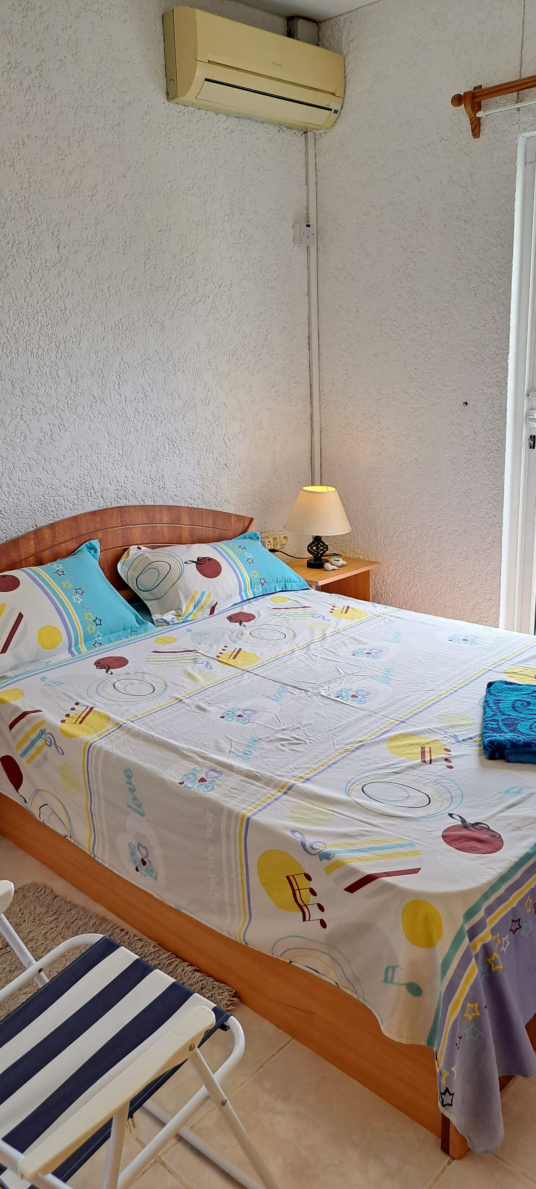 Een bed met een kleurrijk sprei, een bedlamp en een houten hoofdbord.