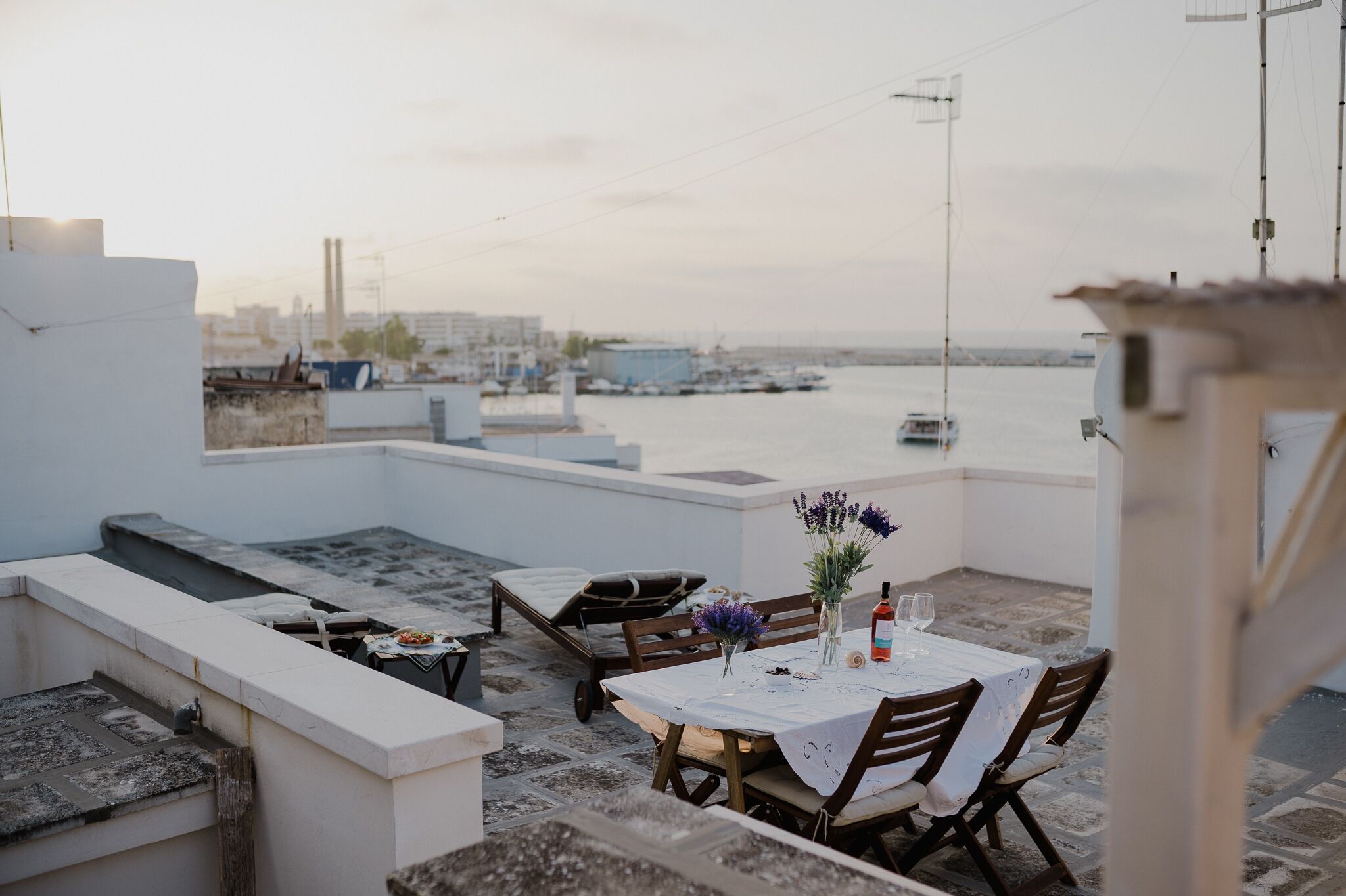 Une terrasse sur le toit, avec une table dressée pour deux, donnant sur une marina où sont amarrés des bateaux.