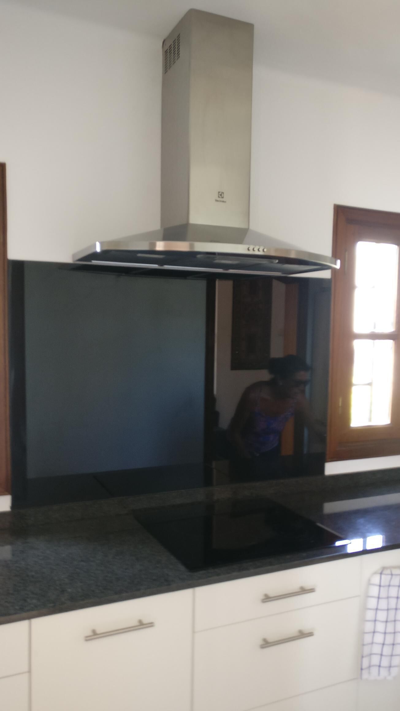 A kitchen with a stainless steel range hood, a black induction cooktop, white cabinets, and a window with curtains.