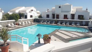 A rooftop swimming pool with lounge chairs, potted plants, and a clear view of the surrounding buildings.