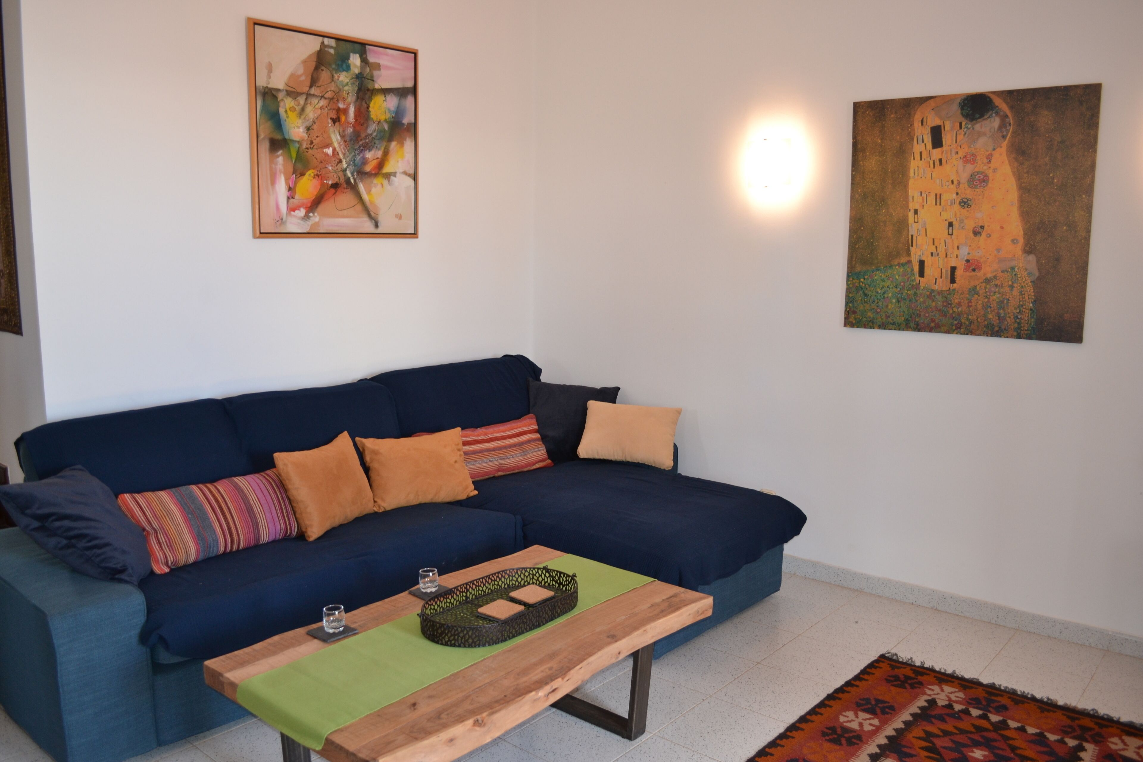 Un salon avec un canapé bleu foncé, des coussins colorés, une table basse en bois et deux tableaux accrochés au mur.