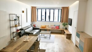 A modern living room with a sofa, a coffee table, a wooden dining table, and a built-in bench with cushions. - CENTRAL = BEAUTIFUL Area ; MODERN BRIGHT Apartment (Paris)
