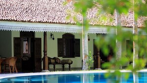 A poolside view of a traditional building with a tiled roof, wooden doors, and a white lace railing. - Near Galle, recent colonial house, 3 bedrooms, large swimming pool in the park (Galle)