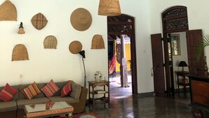 A spacious living room with a high ceiling, a ceiling fan, a sofa with cushions, a coffee table, and decorative woven items on the wall. - Near Galle, recent colonial house, 3 bedrooms, large swimming pool in the park (Galle)