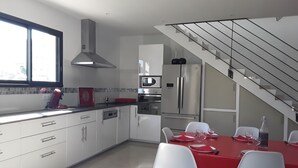 Una cocina moderna con armarios blancos, un refrigerador de acero inoxidable y un comedor con una mesa roja y sillas blancas.