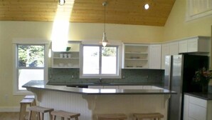A kitchen with wooden cabinets, a large island with stools, and a window providing natural light. - Bright, sunny house w/hot tub, close to beach! (Seaside)
