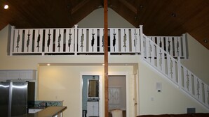 A spacious kitchen with a central island, a dining area with a brown leather couch, and a staircase leading to an upper level. - Bright, sunny house w/hot tub, close to beach! (Seaside)