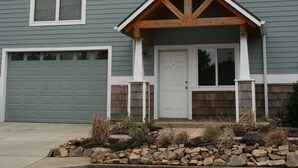 A two-story house with a front porch, a garage, and a stone foundation. - Bright, sunny house w/hot tub, close to beach! (Seaside)
