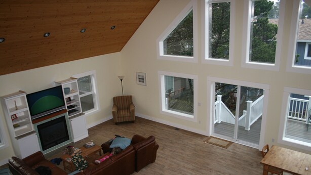 A spacious living room with a large TV, a brown leather sofa, and a dining table. - Bright, sunny house w/hot tub, close to beach! (Seaside)