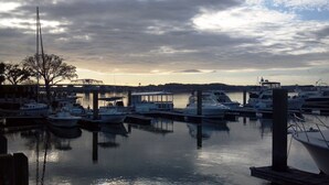 Ein Yachthafen mit anlegenden Booten, eine Brücke im Hintergrund und eine ruhige Wasseroberfläche, die den Himmel spiegelt.