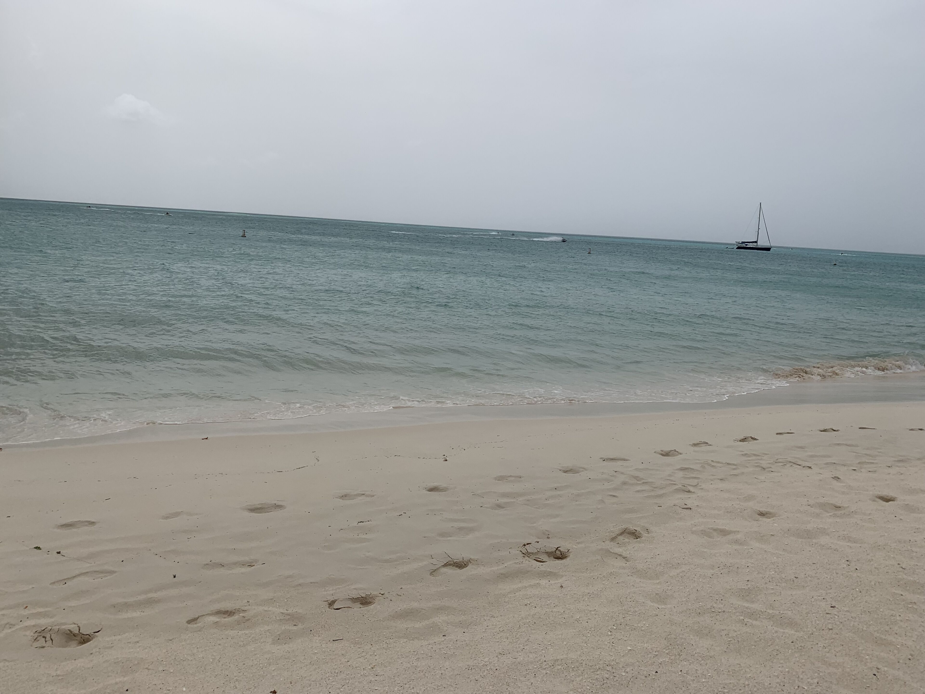 A beach with footprints in the sand and a sailboat in the distance.