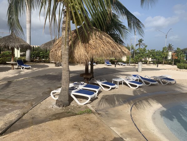 Un complexe hôtelier en bord de mer, doté de parasols en chaume, de chaises longues et de palmiers.