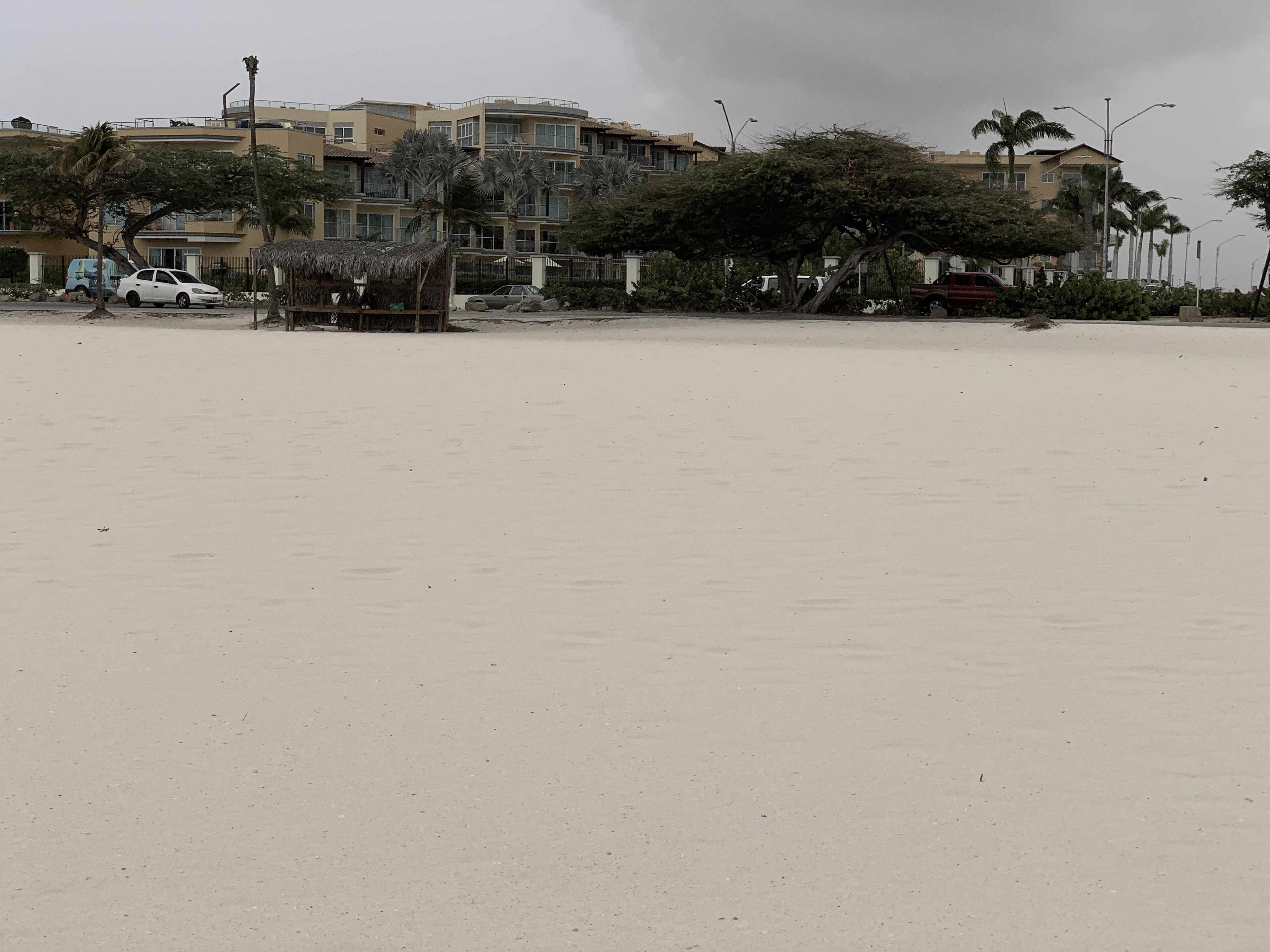 A beachfront property with multiple-story buildings, a sandy beach, and palm trees.