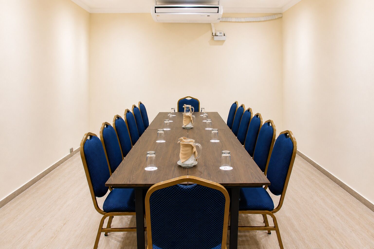 Een vergaderzaal met een lange tafel, blauwe stoelen en een koffiepot.