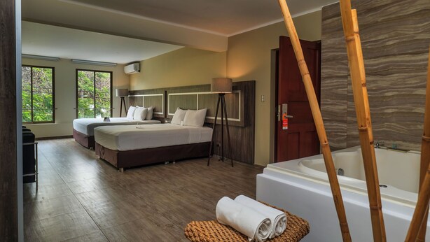 A modern hotel room with two beds, a large bathtub, and a view of greenery through the windows. - Rado Hotel - Quintanas (Trujillo)
