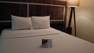 Een keurig opgemaakt bed met witte lakens en kussens, een nachtkastje met een lamp, en een klein informatief kaartje op het bed.