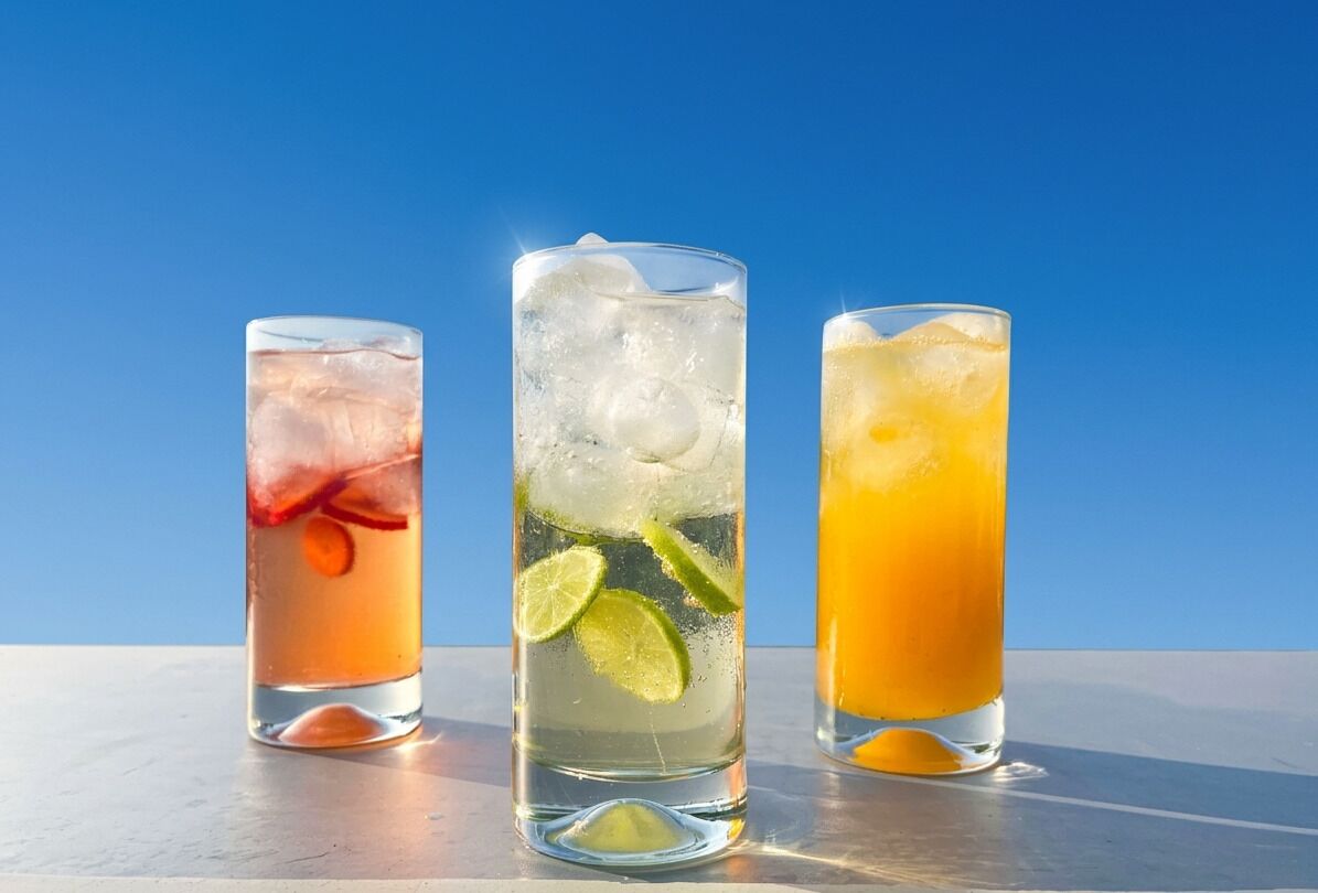 Three glasses of beverages with ice cubes and lime slices.