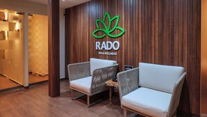 A reception area with a wooden wall, a logo for RADO SPA & WELLNESS, and two wicker chairs with white cushions. - Rado Hotel - Quintanas (Trujillo)